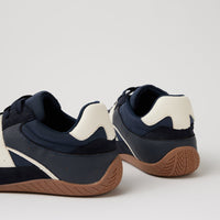 A pair of low-top sneakers shown from the rear three-quarter angle, featuring navy blue and off-white leather uppers with a brown gum sole, set against a plain light gray background.
