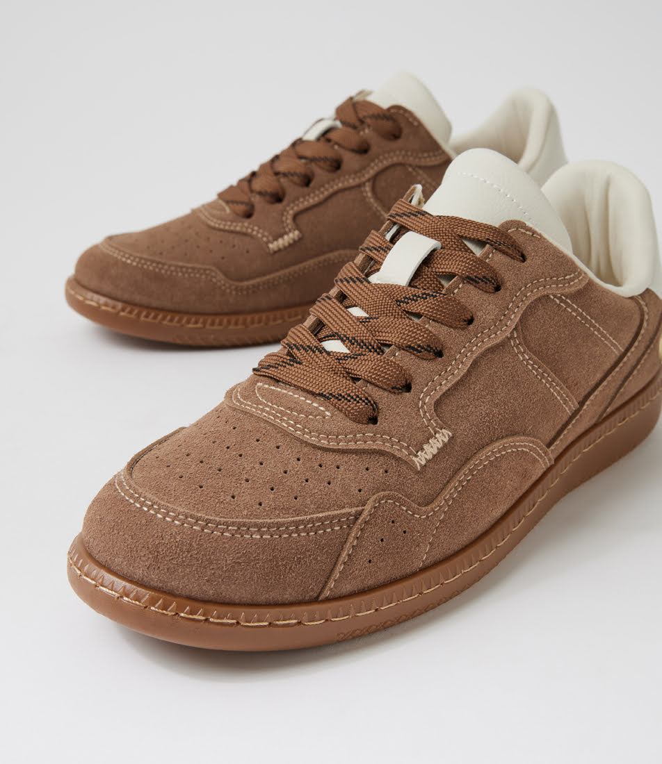 A pair of low-top brown suede sneakers with matching brown laces, white interior lining, and a gum-colored sole, photographed on a clean light gray studio background.