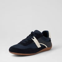A low-top sneaker in navy blue suede and synthetic fabric, featuring a contrasting off-white side stripe, navy laces, and a brown gum sole, shown against a light gray studio background.