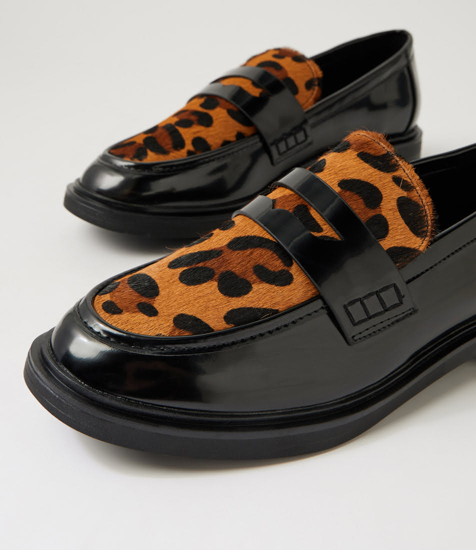 A pair of black patent leather penny loafers featuring a brown and black leopard print fur upper, photographed on a clean white studio background.