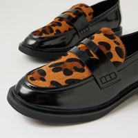 A pair of black patent leather penny loafers featuring a brown and black leopard print fur upper, photographed on a clean white studio background.
